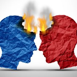 An image showing two male heads on profile that are made of paper. They are facing one another as if in conflict. The one on the left is blue while the one on the right is red. Both paper heads are on fire. 