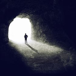 Man standing at cave entrance watching the light at the end of the tunnel