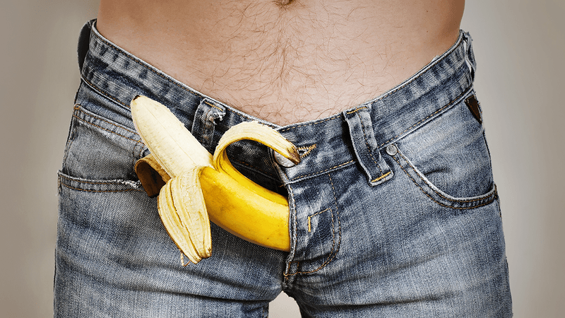 A banana poking out of a man's jean fly.